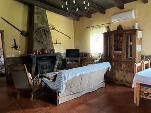 Una sala de estar acogedora con chimenea de piedra, televisor, aparador de madera y zona de comedor.