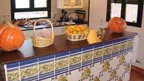 Eine Küchenarbeitsplatte mit dekorativen Kürbissen, einer Orangekorb und einer Flasche.