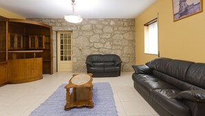 A living room with a stone wall, a wooden cabinet, a black leather sofa, and a wooden coffee table. - Quinta da Vinagra, sunny and modest space for up to 6 people (arcos de valdevez)