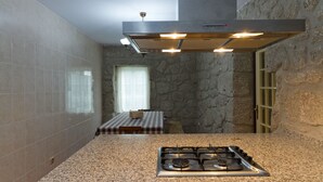 A kitchen with a granite countertop, a gas stove, a stone wall, and a window with a checkered tablecloth. - Quinta da Vinagra, sunny and modest space for up to 6 people (arcos de valdevez)