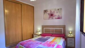 Une chambre à coucher avec une courtepointe aux couleurs vives, une armoire en bois et un tableau floral accroché au mur.