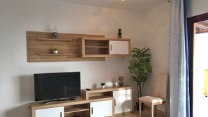 Un salon moderne avec un téléviseur à écran plat, des meubles en bois, une petite table et une plante en pot.