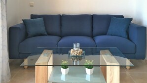 Un salon moderne avec un canapé bleu, une table basse en verre et trois tableaux encadrés accrochés au mur.