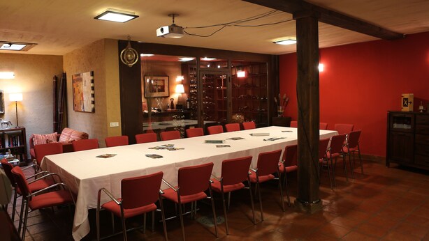 Uma sala de conferências com uma mesa comprida, cadeiras vermelhas e toalha de mesa branca.