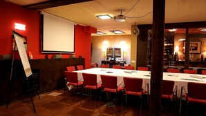 Uma sala de conferência com uma mesa branca, cadeiras vermelhas, uma tela de projetor e um quadro branco.