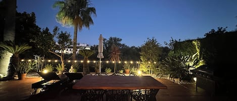 An outdoor dining area with a table and chairs, surrounded by potted plants and a palm tree.