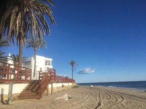 Een strand met een trap naar een gebouw, palmbomen en de oceaan.
