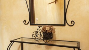 A bathroom with a mirror, a glass table, and a decorative vase with flowers.