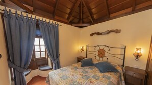 A bedroom with a bed, curtains, a nightstand, wall sconces, and a wooden ceiling.