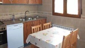 Une cuisine compacte avec des meubles en bois, un lave-vaisselle blanc et une table à manger avec des chaises.