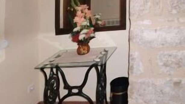 Une pièce avec une table en verre, un vase de fleurs, une poubelle noire et une fenêtre donnant sur un beau paysage.
