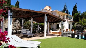 Een villa met een overdekt terras, buitenmeubels en een zwembad.