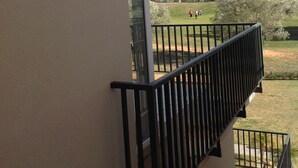 A balcony with a black railing overlooking a grassy area with trees and a clear sky. - Panoramic apartment in Sports & Golf Resort (Sant Jordi)