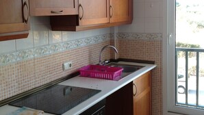 A kitchen with wooden cabinets, a black stove, and a window with a view of the outdoors. - Panoramic apartment in Sports & Golf Resort (Sant Jordi)