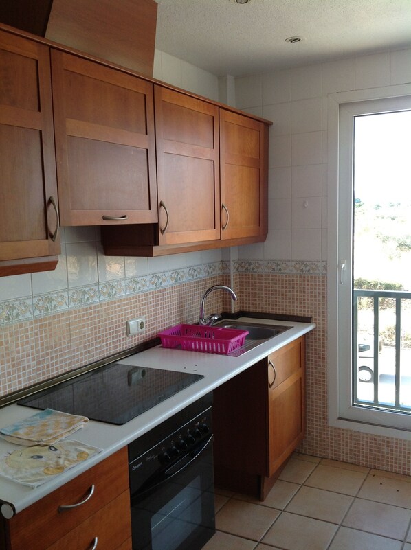 A kitchen with wooden cabinets, a black stove, and a window with a view of the outdoors. - Panoramic apartment in Sports & Golf Resort (Sant Jordi)