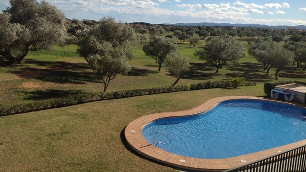 A swimming pool with a tiled edge, surrounded by a grassy area and trees. - Panoramic apartment in Sports & Golf Resort (Sant Jordi)