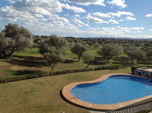 A swimming pool with a tiled edge, surrounded by a grassy area and trees. - Panoramic apartment in Sports & Golf Resort (Sant Jordi)