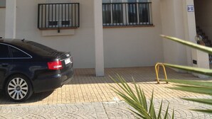A multi-story building with balconies, a car parked in front, and a paved entrance area. - Panoramic apartment in Sports & Golf Resort (Sant Jordi)