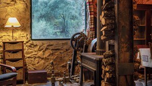 A rustic interior with a stone wall, a large window with a forest view, a wooden chair, a table, and a fireplace. - Mill rehabilitated with Natural Pool and Barbecue in natural environment  (Pinofranqueado)