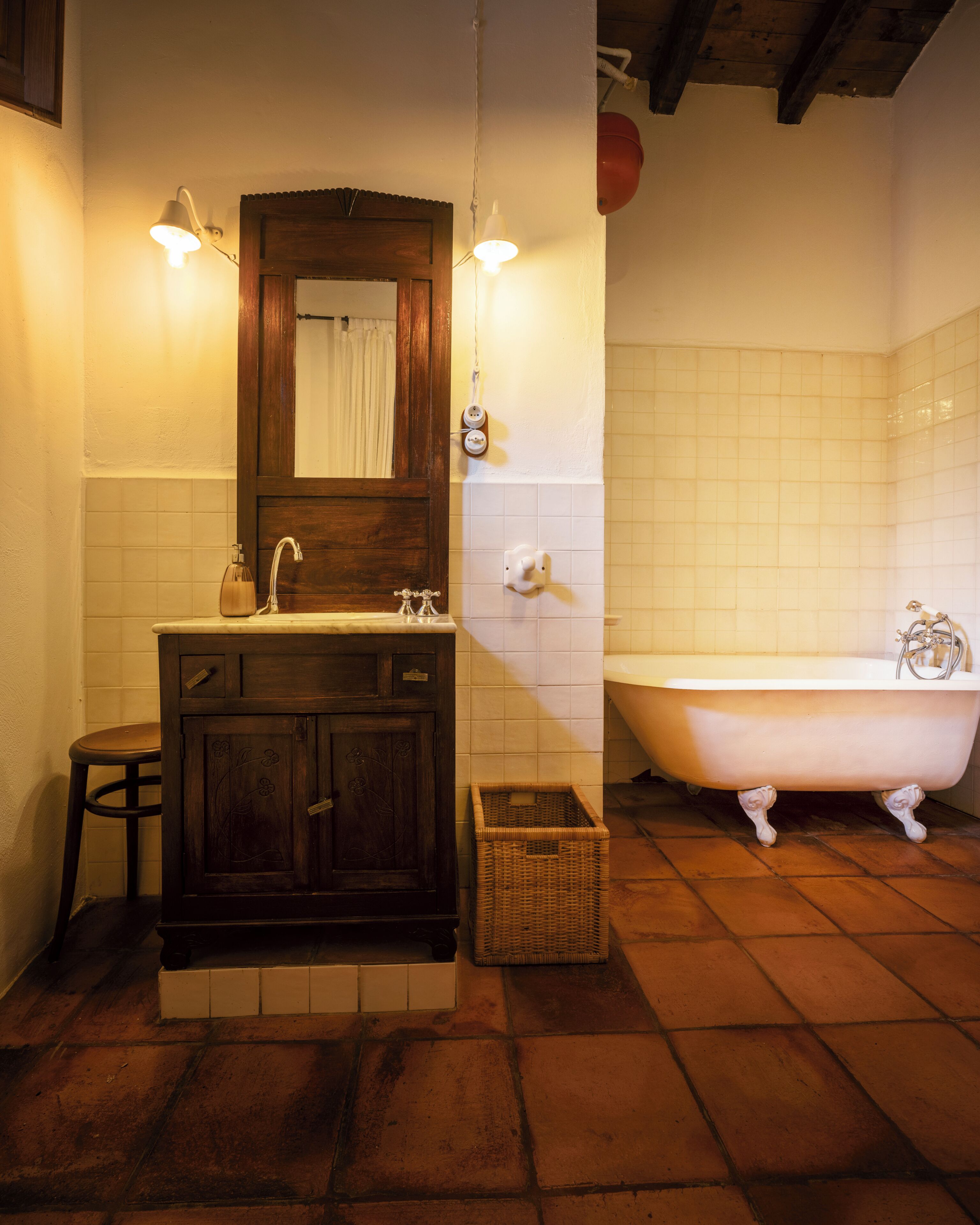Een badkamer met een houten wastafelmeubel, een wit bad en een rieten mand.