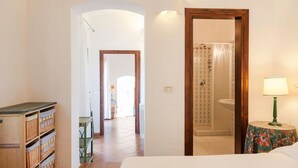 A hotel room with a bed, a bedside table with a lamp, a wooden cabinet, and a bathroom visible through an open door. - LA VILLA GIULIA IN PORTO CERVO (OLBIA TEMPIO)