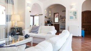 A living room with white sofas, a glass coffee table, and a lamp. There are arched doorways leading to other rooms. - LA VILLA GIULIA IN PORTO CERVO (OLBIA TEMPIO)