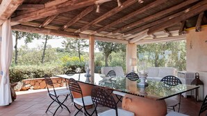 An outdoor patio with a glass table and chairs, surrounded by stone walls and a wooden ceiling. - LA VILLA GIULIA IN PORTO CERVO (OLBIA TEMPIO)