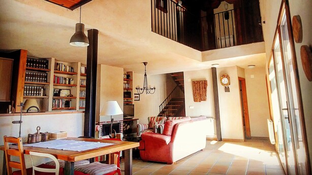 Un vaste espace de vie doté d’un haut plafond, de poutres en bois, d’une cheminée, d’un escalier et d’une grande fenêtre.