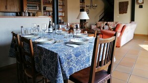 Un coin repas avec une table dressée pour quatre personnes, entourée de chaises en bois. On aperçoit une bibliothèque remplie de livres au fond.