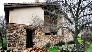 Un bâtiment rustique en pierre, doté d’une petite porte en bois, d’une pile de bois de chauffage et d’une enseigne indiquant qu’il s’agit d’une maison de campagne.