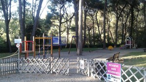 Um parquinho com diversas estruturas de recreação, cercado por uma grade, uma placa indicando reserva para moradores e um banco de madeira.
