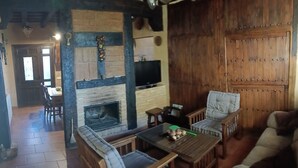 A cozy living room with a fireplace, wooden furniture, and a television. - The House of the Chickens for 4 people (Turrubuelo)