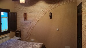 A room with a bed, a brick wall, a wooden ceiling, and a window with curtains. - The House of the Chickens for 4 people (Turrubuelo)