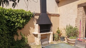 An outdoor patio with a glass table and chairs, a brick barbecue grill, and potted plants. - The House of the Chickens for 4 people (Turrubuelo)