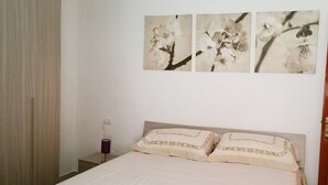 Un dormitorio con una cama, una mesita de noche, una lámpara y tres cuadros florales colgados en la pared.