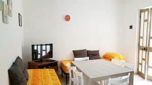 Un espacio habitable compacto con sofá, una mesa de comedor con sillas, televisor y un reloj en la pared.