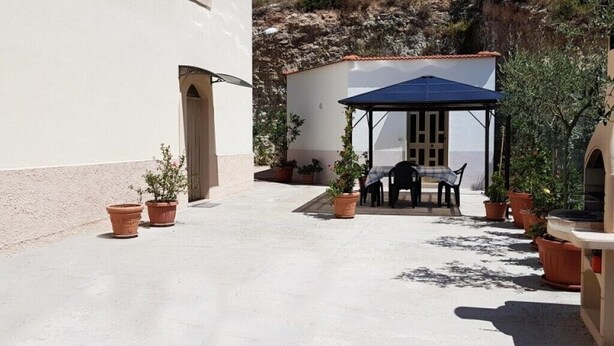 Un patio al aire libre con una zona de estar cubierta, plantas en macetas y vistas al mar.