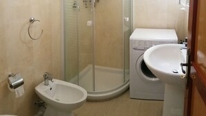 Un baño con ducha de mampara de vidrio, un bidé, lavadora y lavamanos.