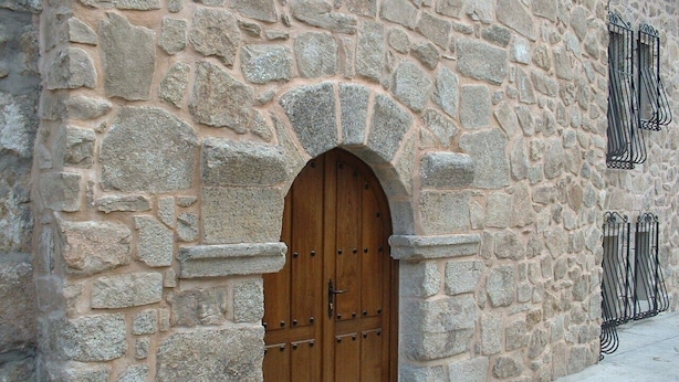 Un edificio in pietra con un'ampia porta di legno e una piccola finestra con inferriate.