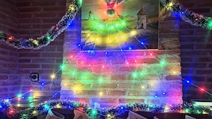 Un camino adornato con luci natalizie colorate e ghirlande, calze con lettere e un quadro incorniciato sopra.