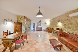 Uma sala ampla com uma mesa de jantar de madeira, cadeiras, um sofá de couro e uma parede decorativa em pedra.