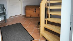 Eine Treppe mit Holzstufen und einem Metallgeländer, eine weiße Tür, eine Holztruhe und eine schwarze Fußmatte.