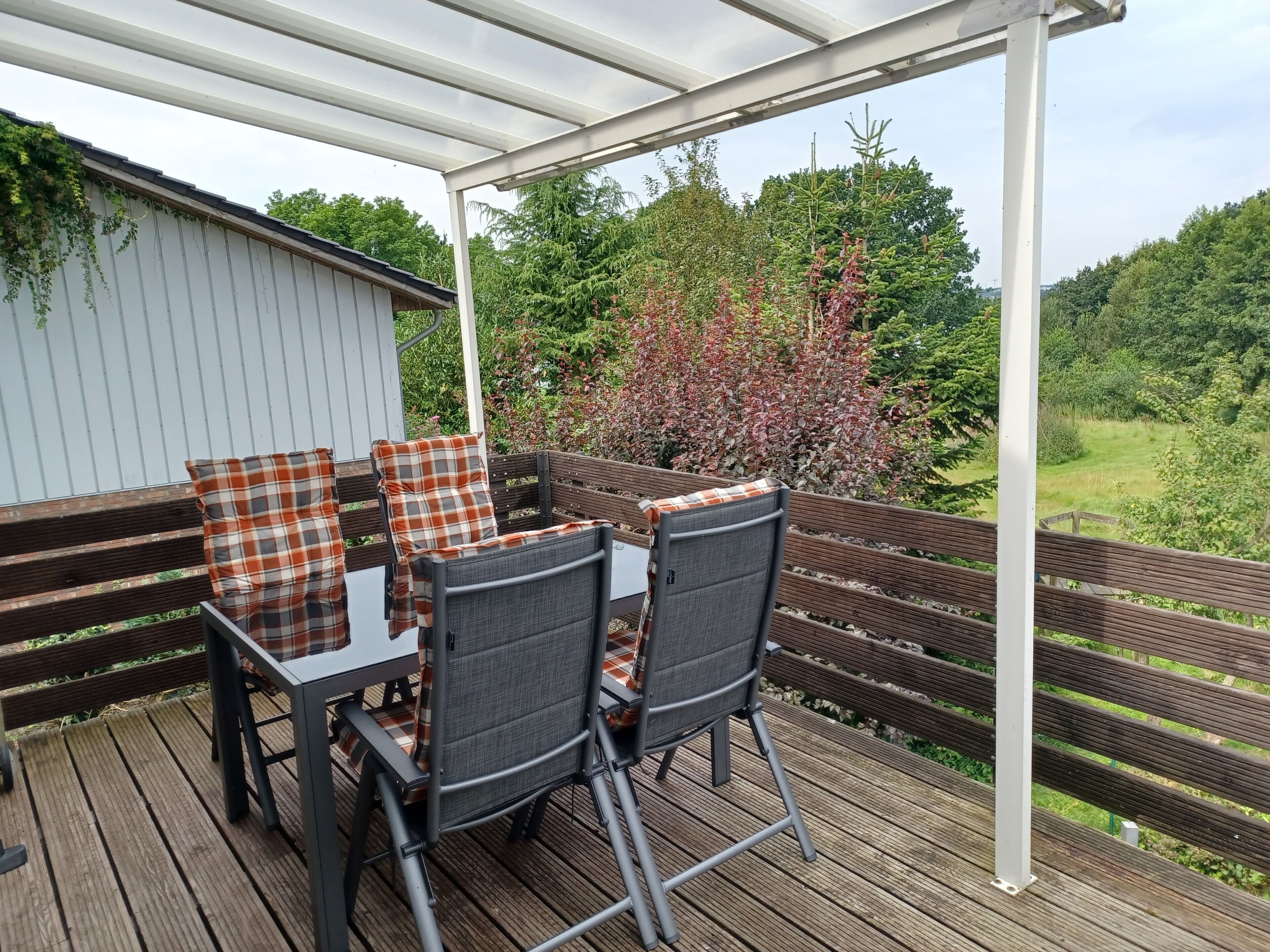 A covered outdoor patio with a table and chairs, surrounded by a wooden deck and a white pergola.