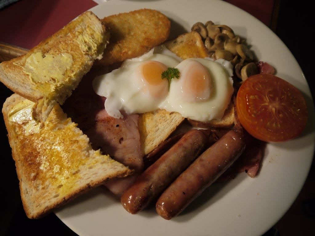 A plate of breakfast food including eggs, sausages, mushrooms, toast, and a tomato.