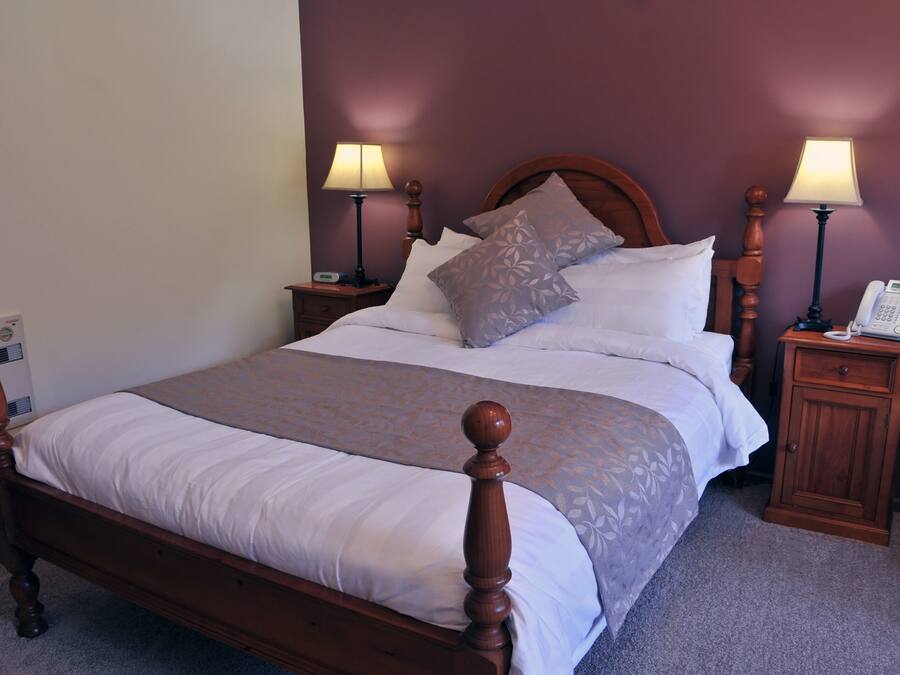 A neatly made bed with a wooden headboard, two bedside tables with lamps, and a telephone on one of the tables.