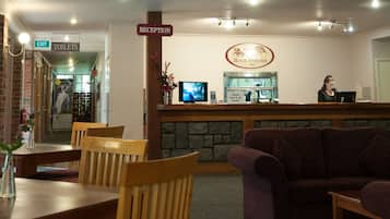 A reception area with a counter, a TV, and a sign for the reception. There are wooden chairs and a sofa.