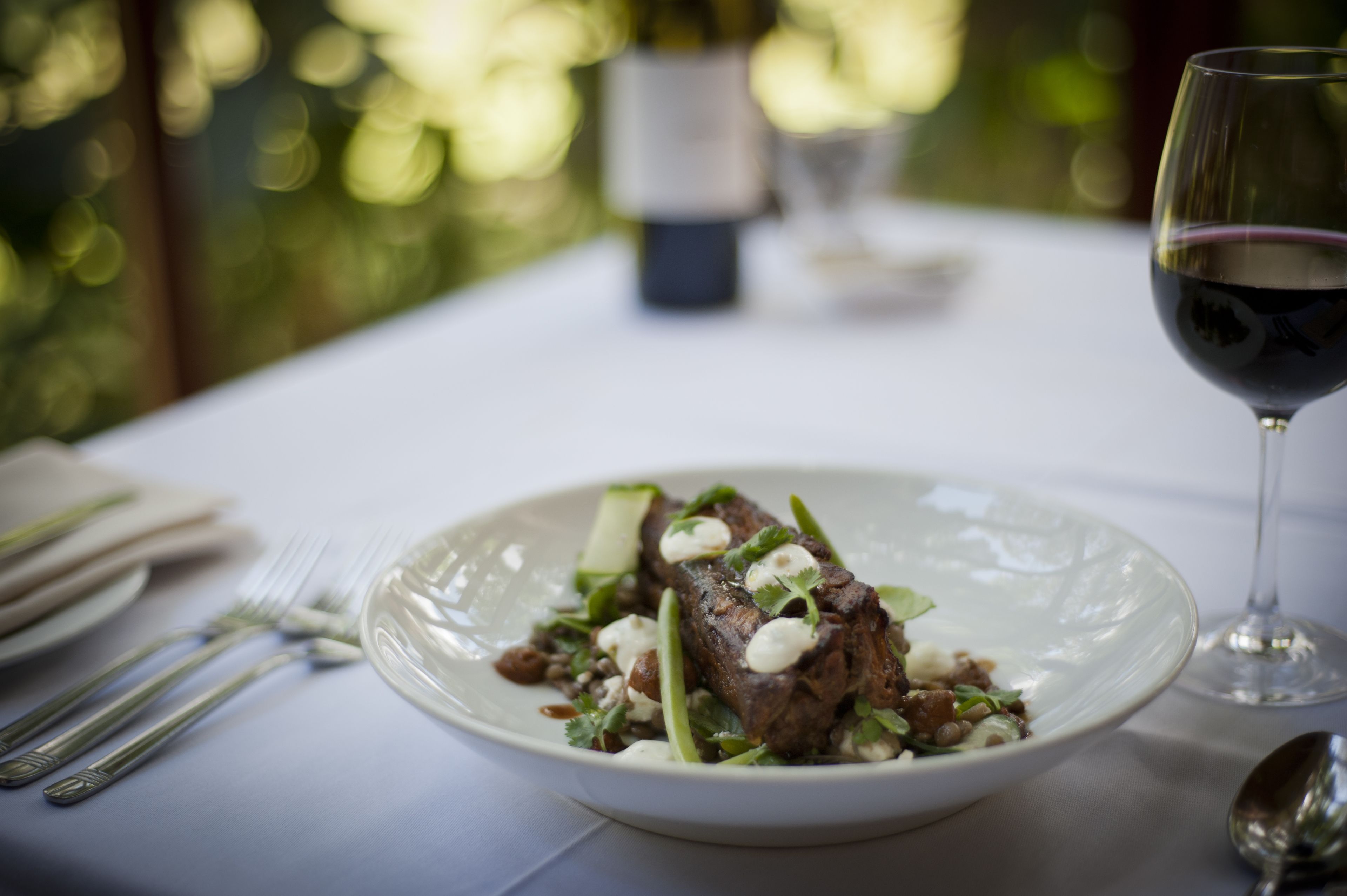 A plate of food on a table with a wine glass and cutlery.