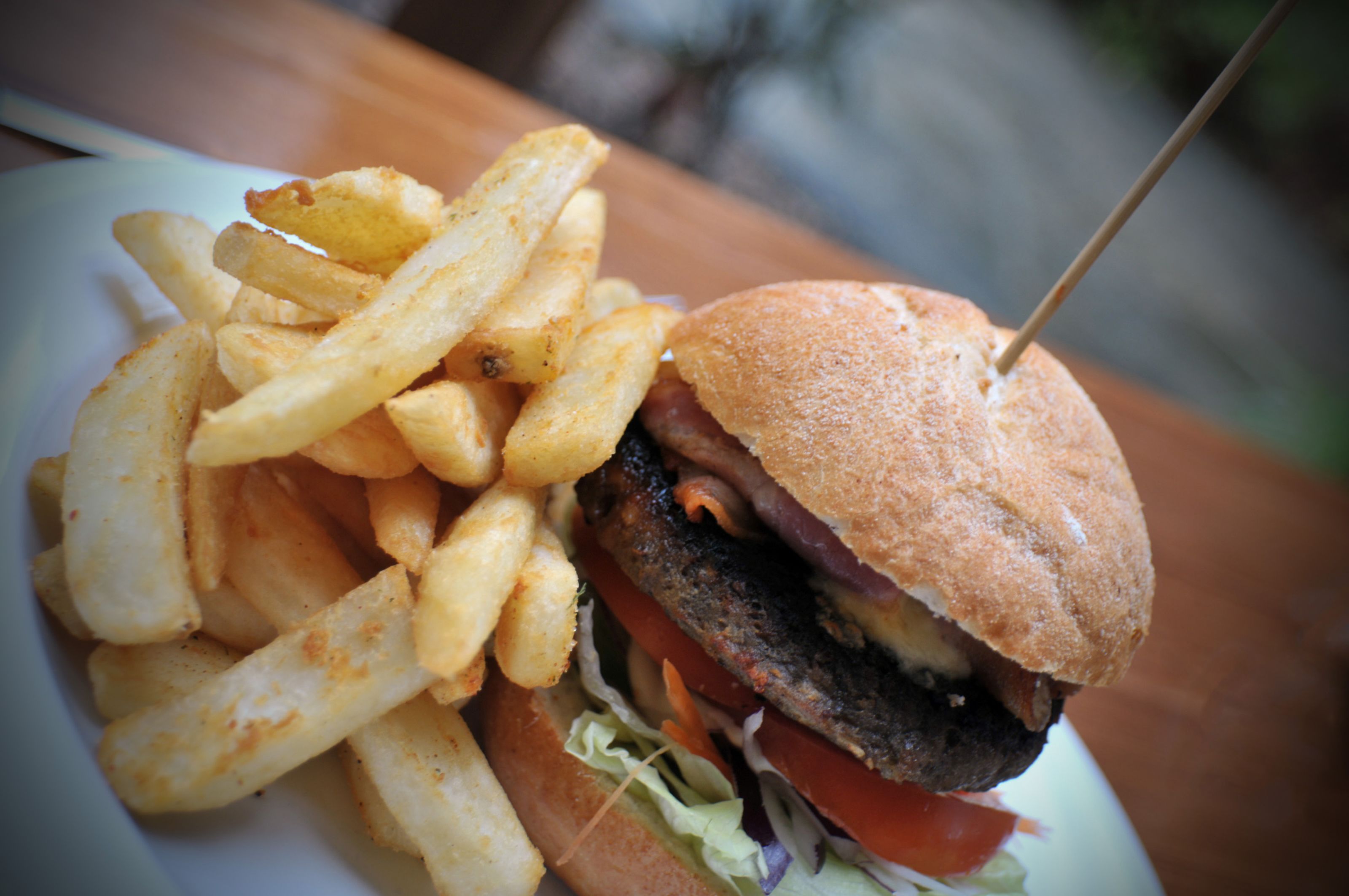 A burger with a toasted bun, lettuce, tomato, and a grilled patty, accompanied by a side of French fries.