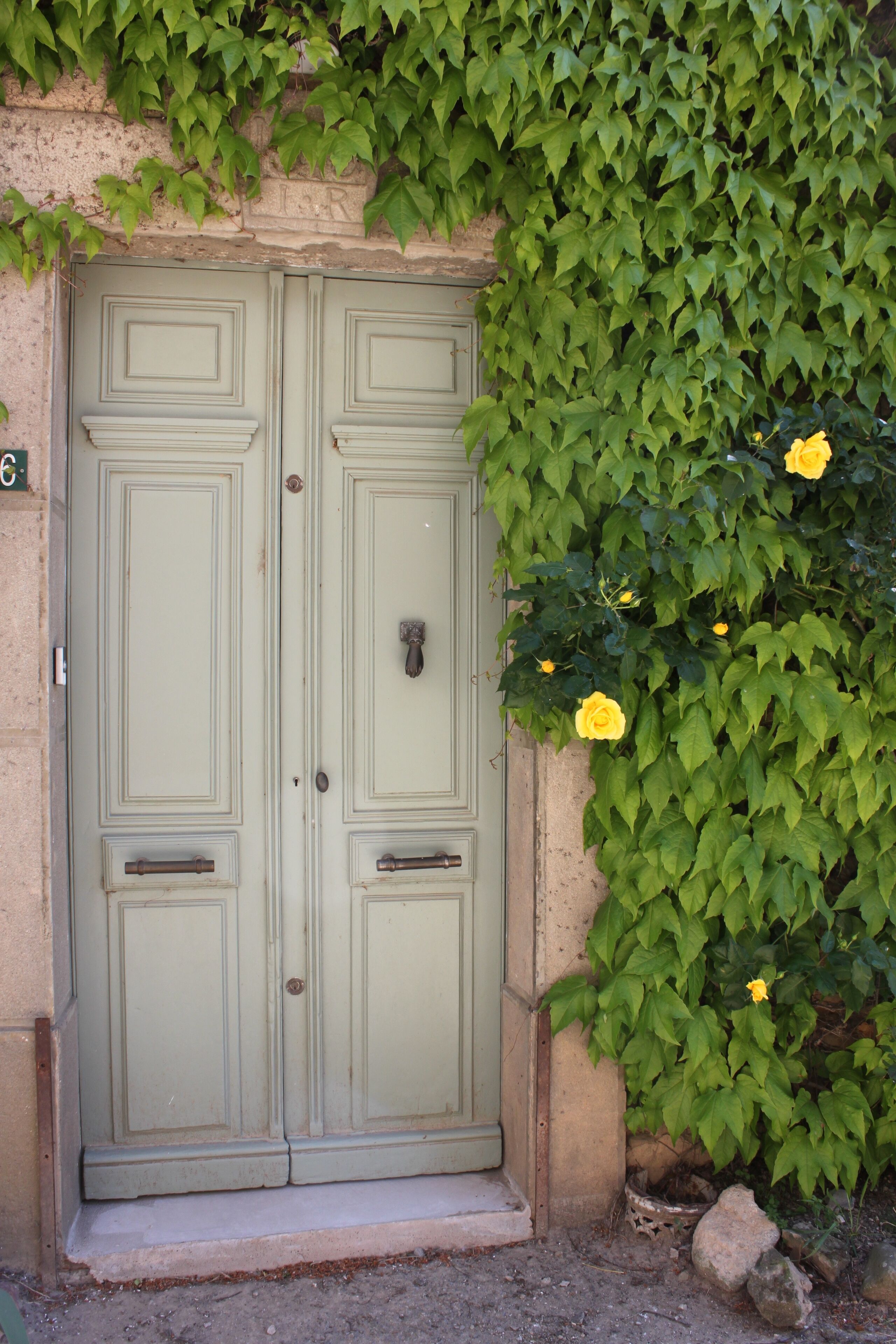 A double door with a simple design, set in a stone wall with ivy and yellow flowers.