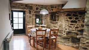 A dining area with a stone wall, a round table with chairs, a pendant light, and a window with a view. - Casa da Labaceira (for 7 people) (Cerdedo)